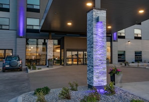 A modern building with a stone pillar, a car parked in front, and a well-lit entrance.