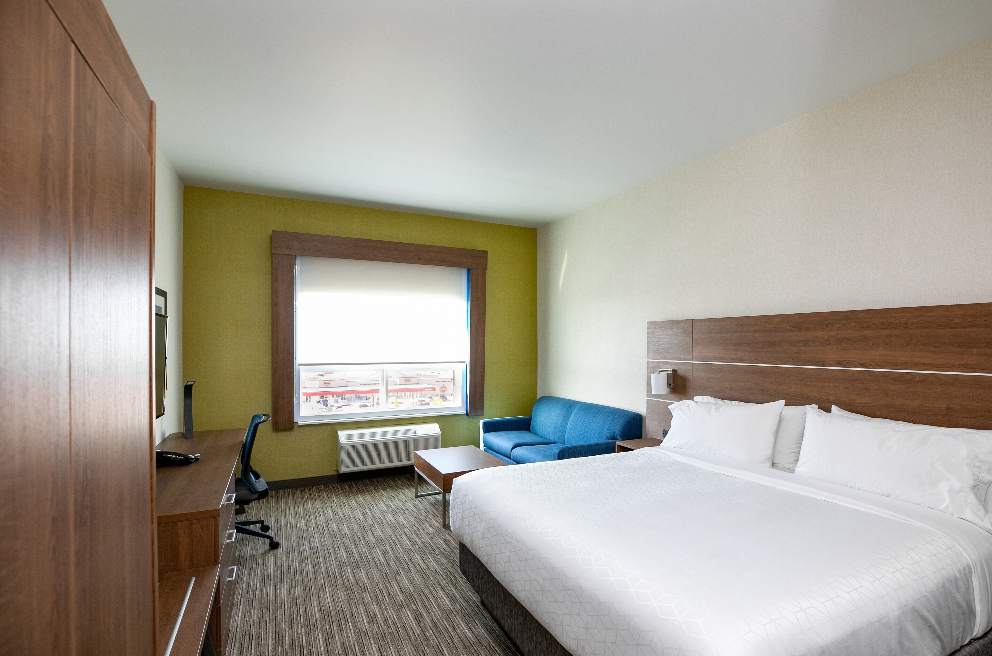 Ein Hotelzimmer mit einem großen Bett, einem blauen Sessel, einem Schreibtisch und einem Fenster mit Blick.