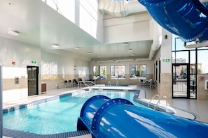 A swimming pool with a water slide, sunroof, and seating area.
