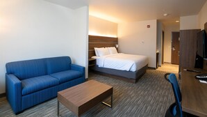 A hotel room with a blue sofa, a bed with white bedding, a wooden coffee table, and a desk with a keyboard and mouse. - Holiday Inn Express Lethbridge Southeast by IHG (Lethbridge)