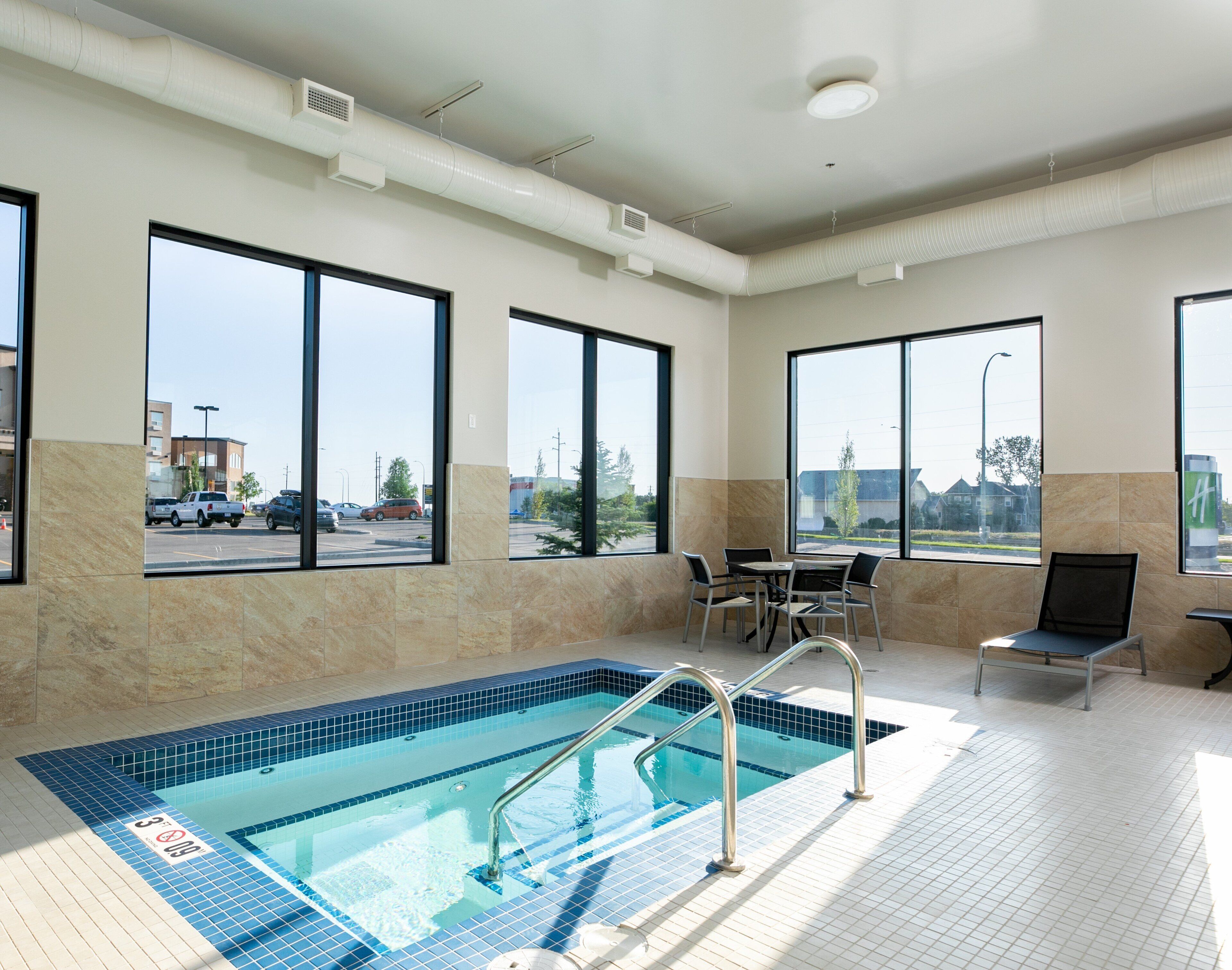 A hotel indoor pool with clear views of the parking lot and buildings outside.