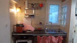 Et kompakt køkken med vask, mikroovn og et lille vindue.