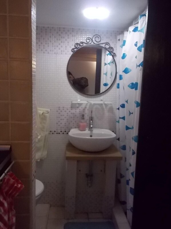 Une salle de bain avec un miroir rond, un lavabo blanc et un rideau de douche bleu à motifs de poissons.