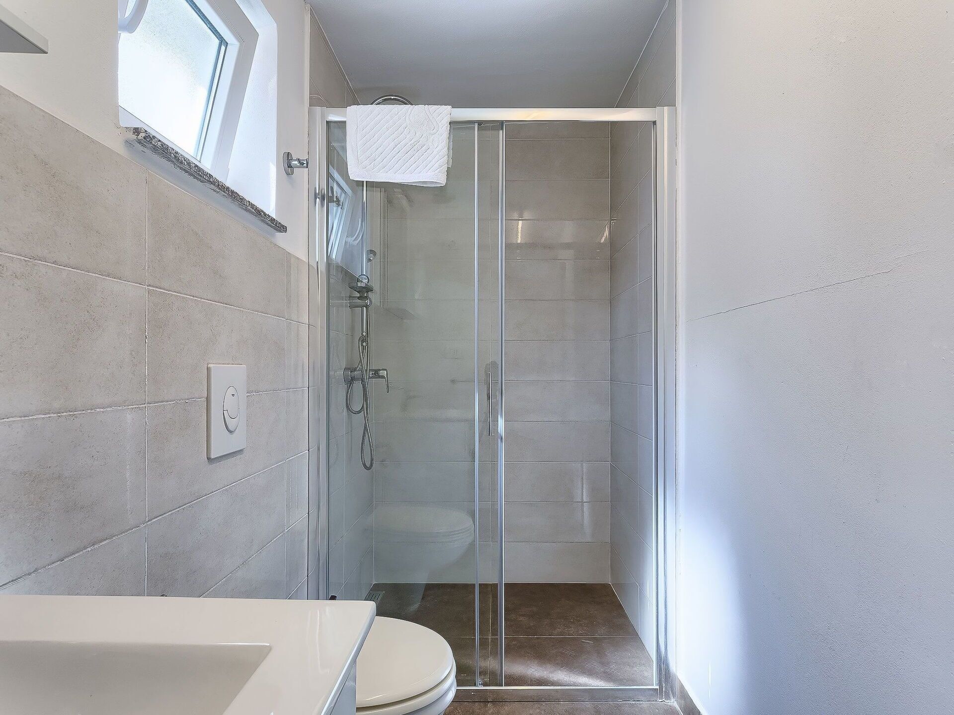 Ein modernes Badezimmer mit Duschkabine aus Glas, einem weißen Waschbecken und einer Toilette.