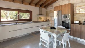 Una cocina moderna con pared de piedra, vigas de madera, un refrigerador de acero inoxidable y una zona de comedor con sillas blancas.