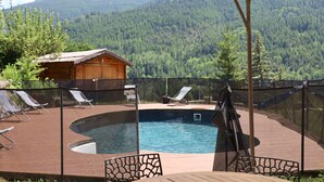 Ein Schwimmbad mit Holzterrasse, Liegestühlen und Blick auf einen bewaldeten Bergkamm.
