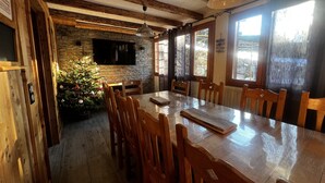 Ein Essbereich mit einem großen Holztisch, Holzstühlen, einer Steinwand, einem an der Wand montierten Fernseher und einem Weihnachtsbaum.