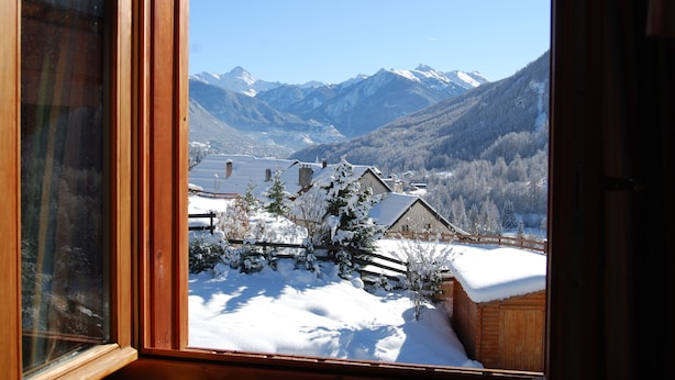 Blick aus einem Fenster eines Berggasthofs auf verschneite Landschaft, hölzerne Zäune und schneebedeckte Berge im Hintergrund.