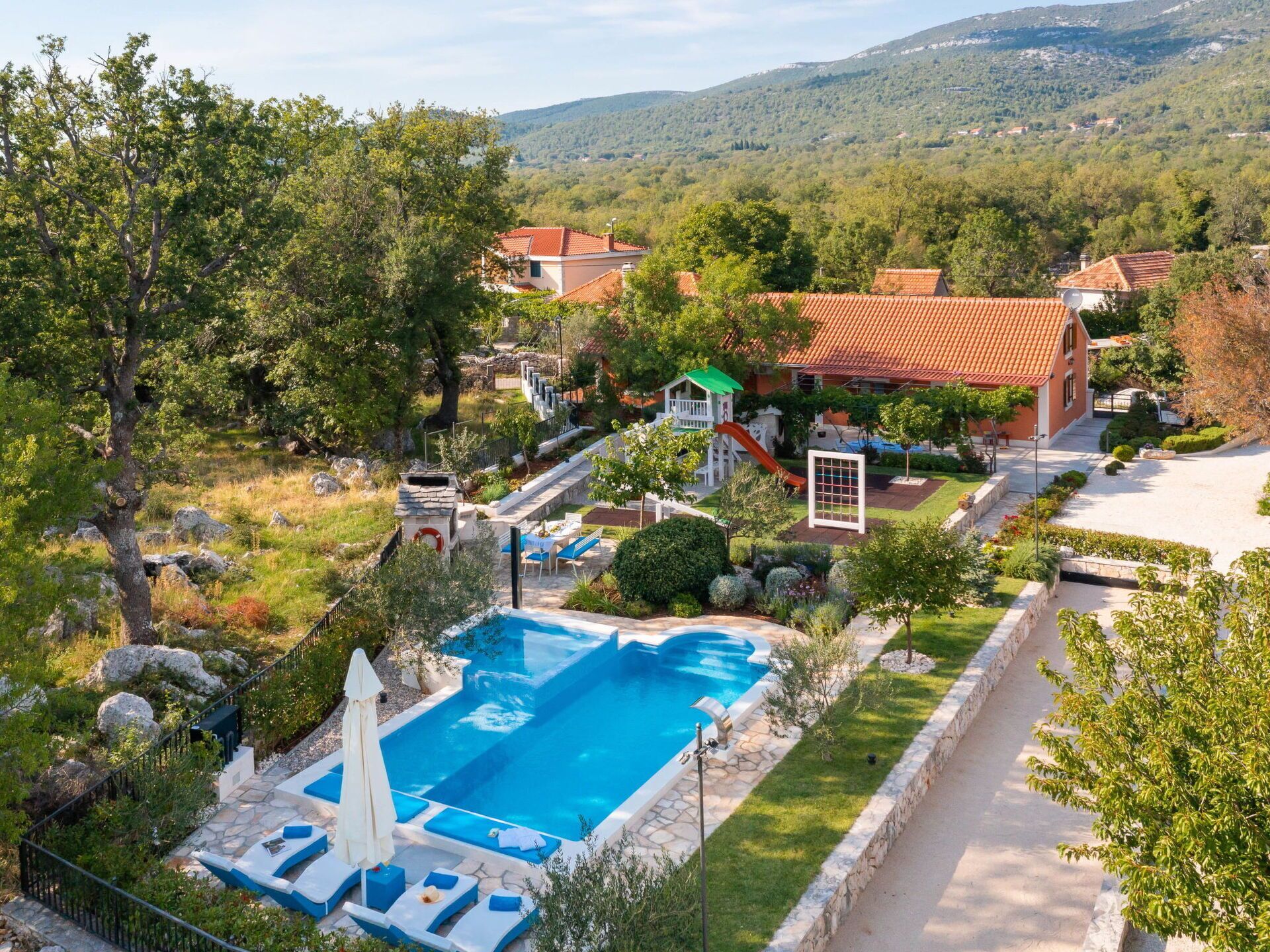 A resort with a swimming pool, a children's play area, and a view of the surrounding hills.