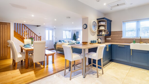 A modern kitchen with a wooden dining table and bar stools, a built-in island, and blue cabinetry. - Stone Lodge, Old Hunstanton, Norfolk (Old Hunstanton)