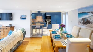 A modern living room with a wooden bench, a dining table set for four, and a kitchen in the background. - Stone Lodge, Old Hunstanton, Norfolk (Old Hunstanton)