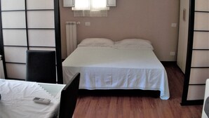 A bedroom with a bed, a chair, a bedside table, a lamp, and a window with curtains. - The attic of Val. Apartment with large terrace, in a period cottage. (Roma)