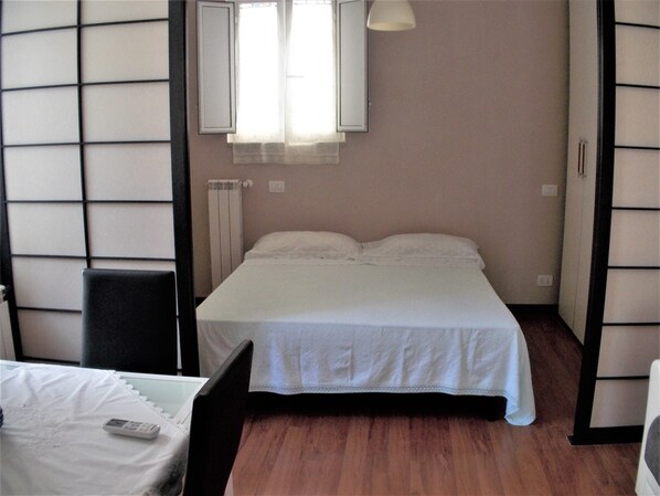 A bedroom with a bed, a chair, a bedside table, a lamp, and a window with curtains. - The attic of Val. Apartment with large terrace, in a period cottage. (Roma)
