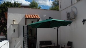 A patio area with a green umbrella, a table, two chairs, a white wall, a tiled roof, and an air conditioning unit. - The attic of Val. Apartment with large terrace, in a period cottage. (Roma)