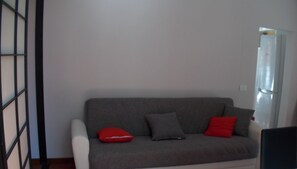 Un canapé gris avec des coussins rouges et gris, un fauteuil blanc et un plancher en bois.