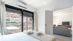 Una habitación de hotel moderna con una cama grande, un balcón con cortinas, un televisor y un sofá.