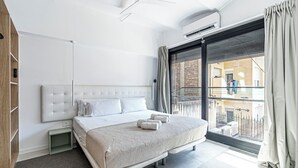 Habitación de hotel moderna con una cama grande, ventilador de techo, unidad de aire acondicionado, vista al balcón exterior y un panel de madera en el lado izquierdo.