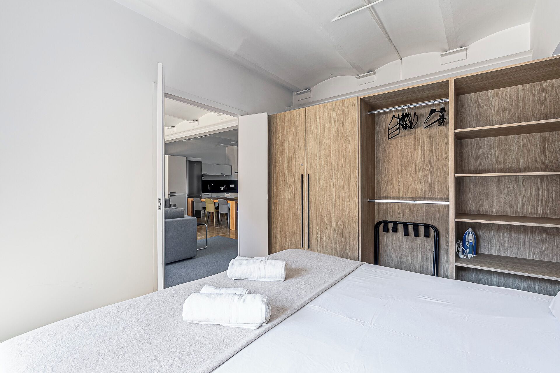Une chambre d’hôtel moderne avec un lit, une armoire en bois et, au fond, une petite cuisine.