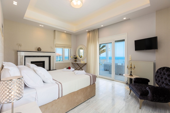 A modern bedroom with a large bed, a fireplace, a balcony with a view, and a flat-screen TV.