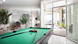 Een moderne binnenzwembadruimte met een groene pooltafel, stoelen en uitzicht op het buitenterras.
