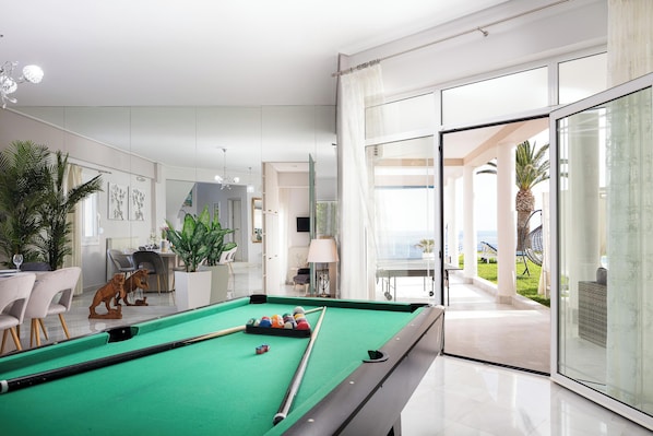 A modern indoor pool area with a green pool table, chairs, and a view of the outdoor patio.