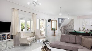Een ruime woonkamer met een grote flatscreen televisie, een beige bank, een witte fauteuil en een salontafel met decoratieve objecten.