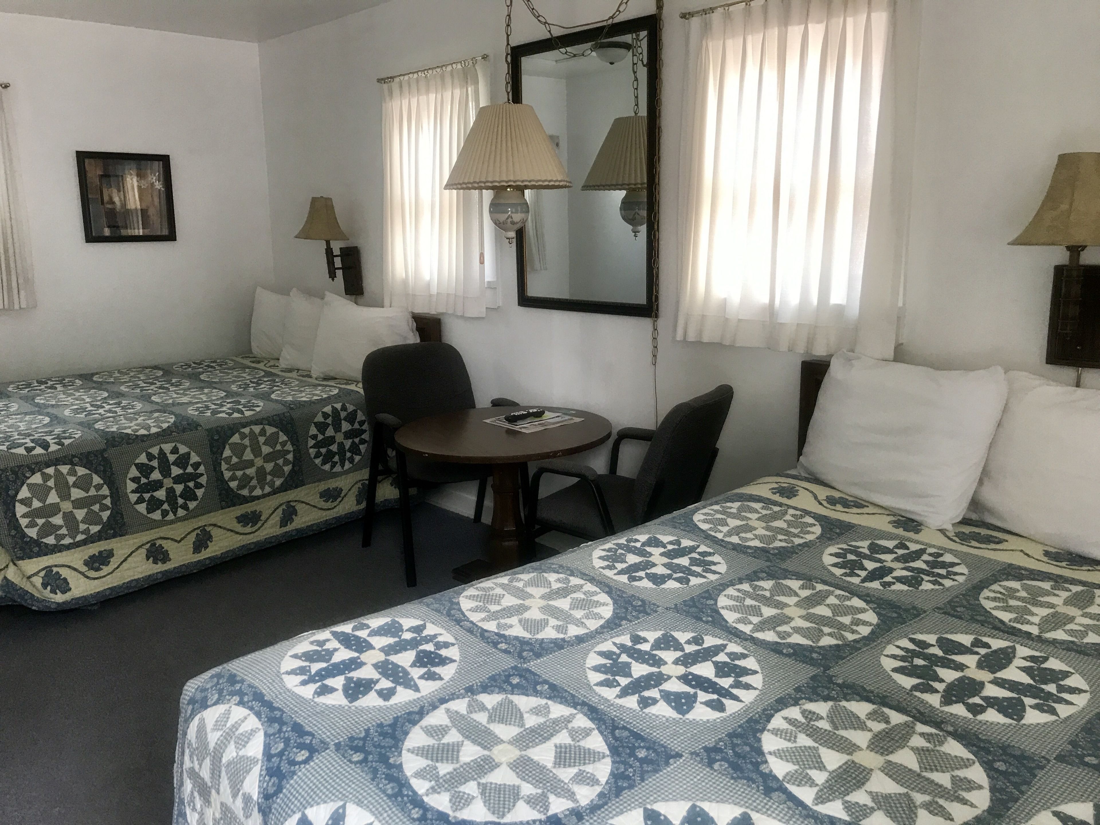 Hotellihuone, jossa on kaksi erillistä sänkyä, pieni pyöreä pöytä, kaksi tuolia, peili ja kaksi lamppua.