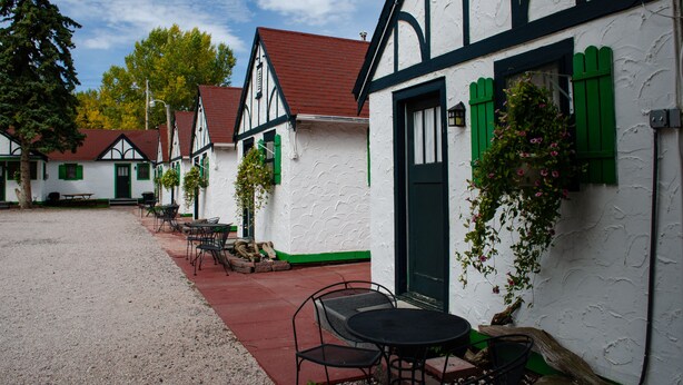 Eine Reihe traditioneller Fachwerkhäuser mit grünen Fensterläden, einem Kieshof und Außenbestuhlung.