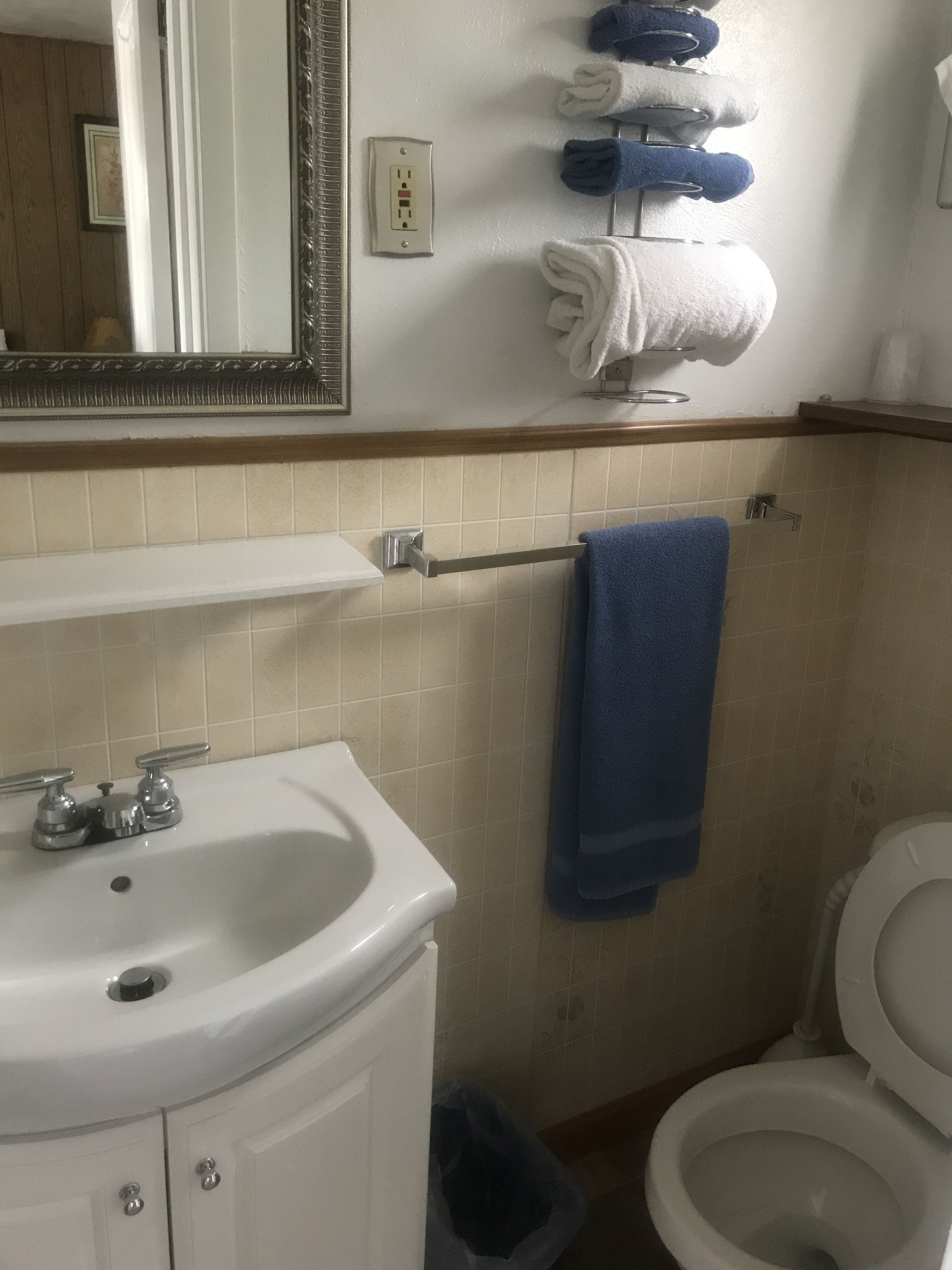 Un baño con lavamanos, espejo, toallero y retrete.