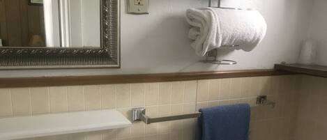Un baño con lavamanos, espejo, toallero y retrete.