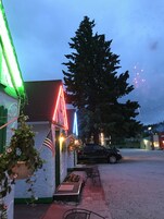Un edificio con un letrero de neón verde, un letrero de neón rojo y una bandera estadounidense. Hay un árbol frente al edificio.