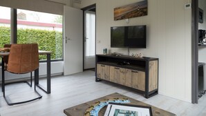 Ein modernes Wohnzimmer mit einem Holzesstisch, einem braunen Sessel, einem an der Wand befestigten Fernseher und einer Kaffeemaschine.