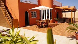 A building with a staircase, a covered patio area with a table and chairs, and potted plants.