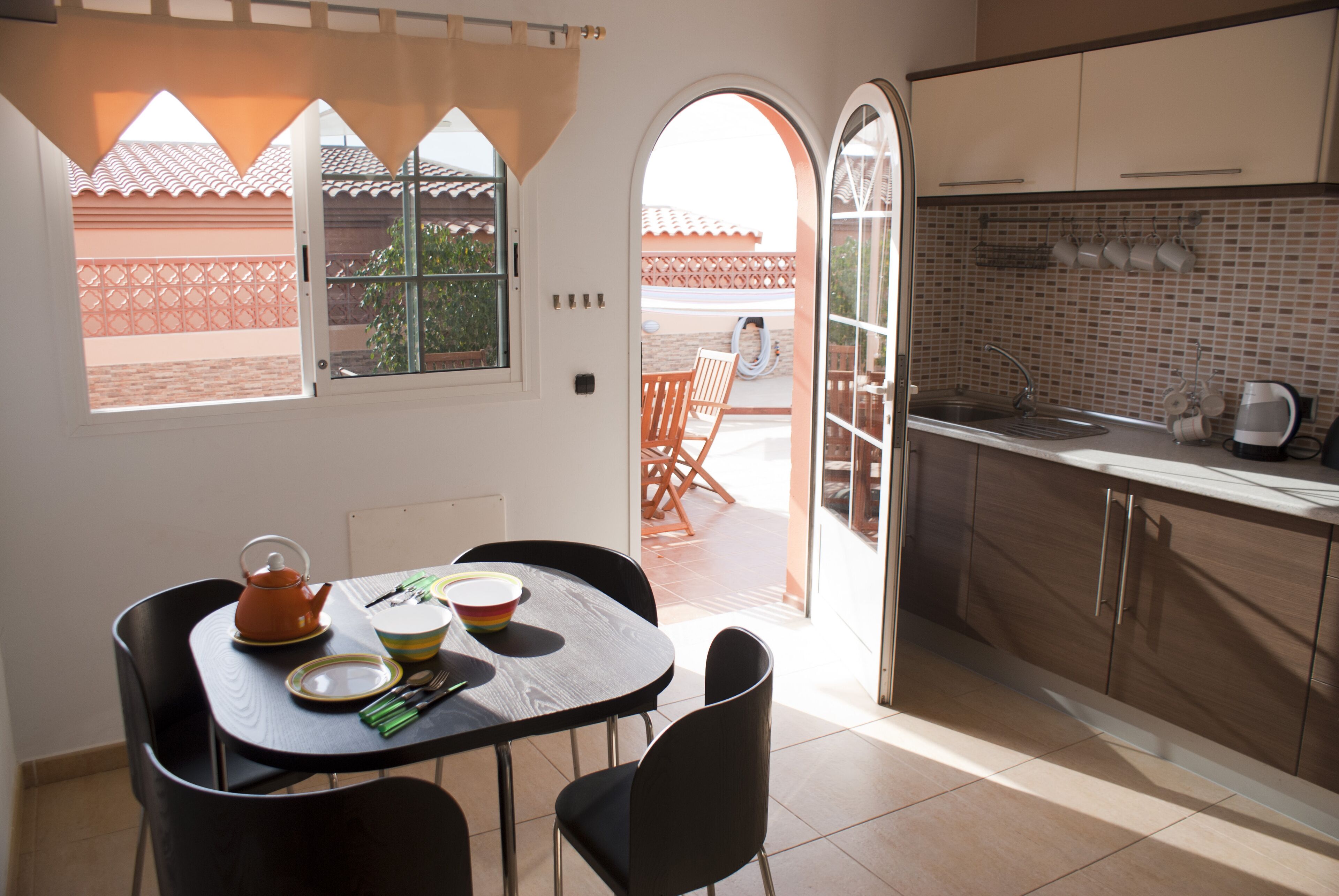 Une cuisine compacte avec un coin repas, une vue dégagée par une porte ouverte et un sol carrelé.