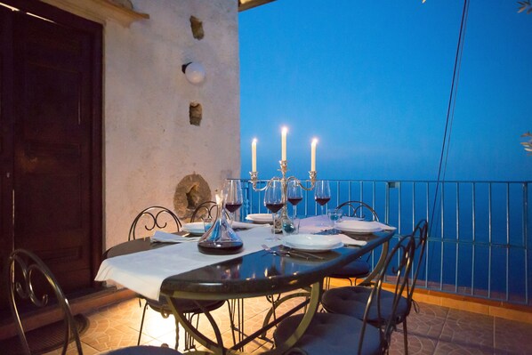 A dining table set with candles, wine glasses, and plates on a balcony with a blue sky view.