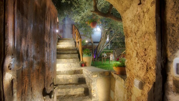 Una escalera de piedra que conduce a una puerta de madera, rodeada de follaje y una maceta colgante.