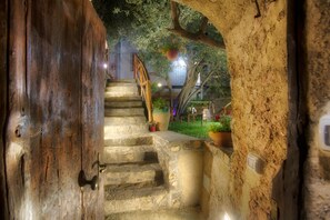 A stone staircase leading to a wooden door, surrounded by greenery and a hanging flower pot.