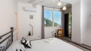 Un dormitorio con una cama grande, una ventana con vistas, una silla y una planta pequeña.