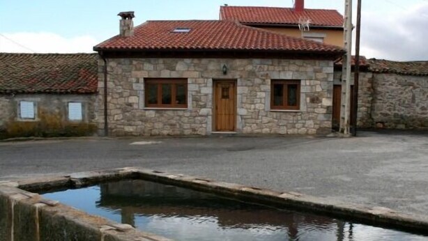 Un edificio in pietra con tetto in tegole, una porta in legno e due finestre. Di fronte all'edificio, una vasca d'acqua rettangolare.