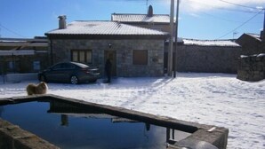 Un edificio in pietra con tetto a tegole, un'auto parcheggiata di fronte e una piccola piscina sullo sfondo.