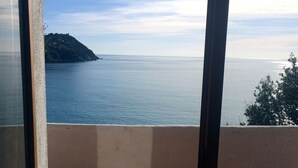 Vista pela janela de uma varanda com vista para um mar calmo e uma ilha distante.