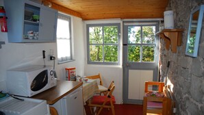 A compact kitchen with a microwave, a small refrigerator, and a wooden table with chairs. There is a window with a view of trees outside. - Bradley Cross Farm, Shepherds Cottage (Cheddar)