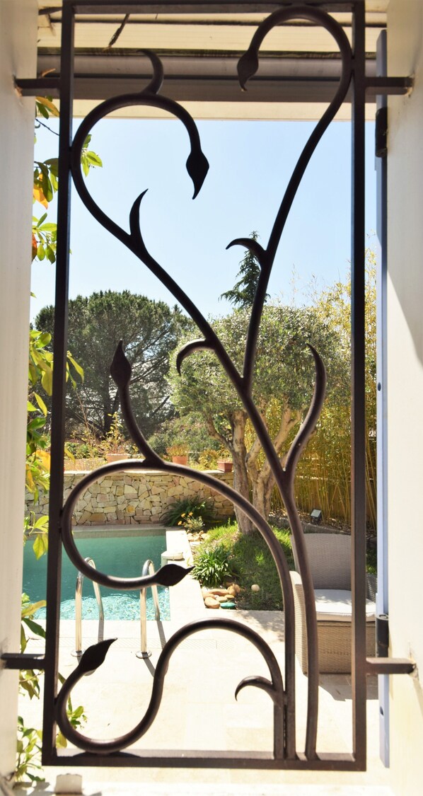 A wrought iron gate with a pool and greenery in the background.