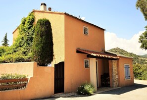 A single-story building with a sloped roof, a small porch, and a stone wall entrance. - Modern Villa with beautiful garden, heated pool, barbeque area, close to beaches (Roquebrune-Sur-Argens)