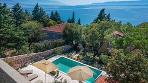 A pool area with two umbrellas, a stone wall, and a view of the sea and mountains. - Wonderful private villa for 6 guests with A/C, private pool, WIFI, TV, terrace and pets allowed (Novi Vinodolski)