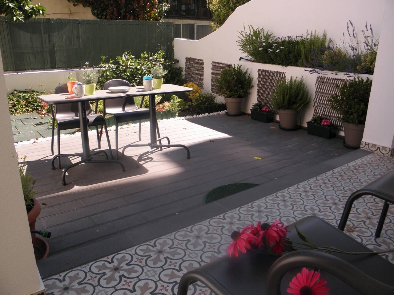 A patio with a table and chairs, surrounded by potted plants and a decorative fence.
