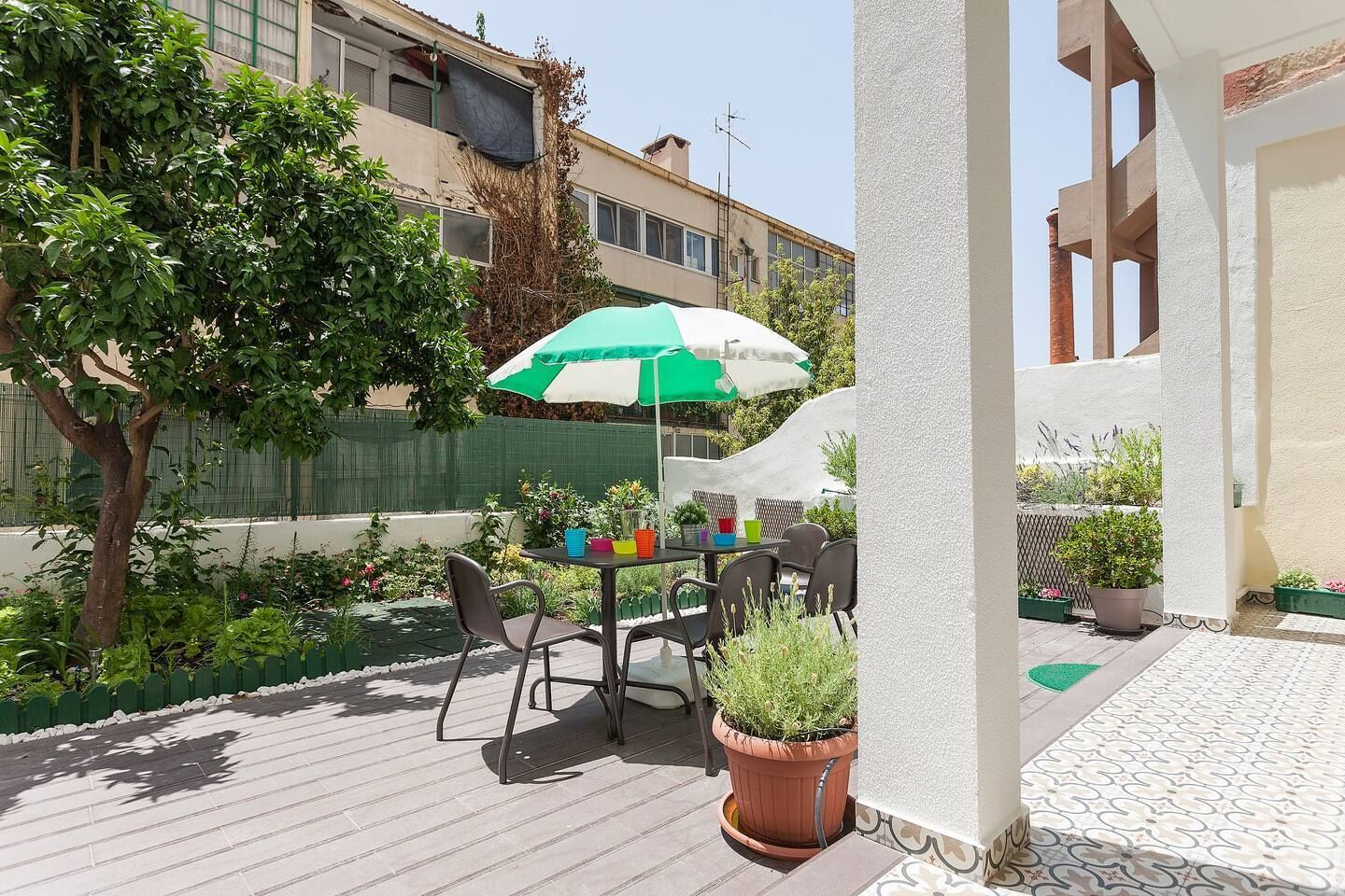 A patio with a table and chairs, a green and white umbrella, and potted plants.