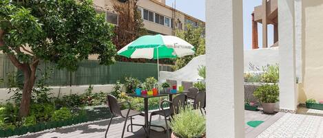 A patio with a table and chairs, a green and white umbrella, and potted plants.