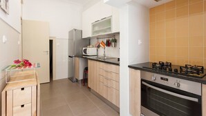 Eine moderne Küche mit Mikrowelle, Herd und Backofen. Ein kleiner Tisch mit einer Blumenvase und einem Stuhl stehen bereit. Die Küche verfügt über weiße Schränke und eine geflieste Spritzschutzwand.