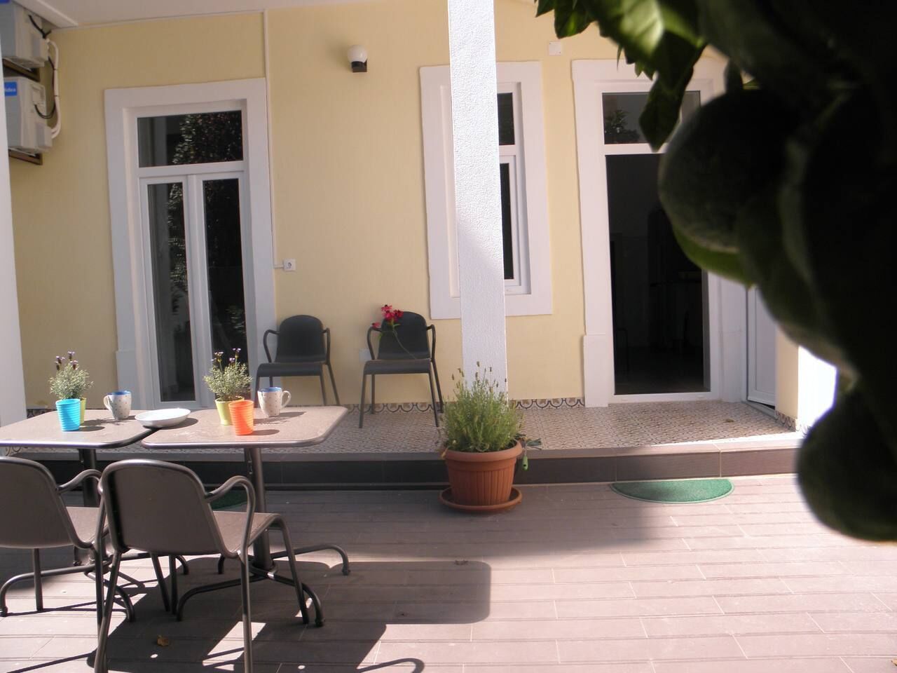 Une terrasse extérieure avec une table et des chaises, un pot de fleurs et une porte avec une fenêtre.
